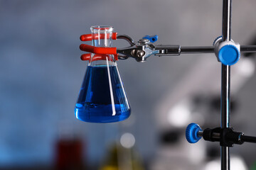 Flask with blue liquid on retort stand in laboratory, closeup
