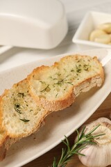 Tasty baguette with garlic, rosemary and dill on table, closeup