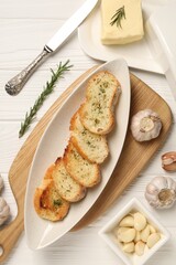 Tasty baguette with garlic and dill served on white wooden table, flat lay