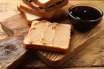 Tasty peanut butter sandwiches and jam on wooden table, closeup