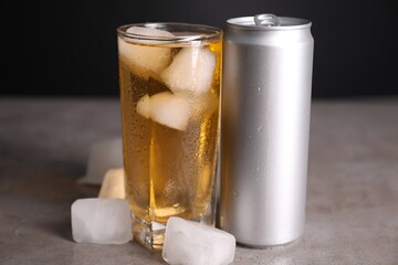 Tasty energy drink with ice cubes in glass and aluminium can on grey table, closeup