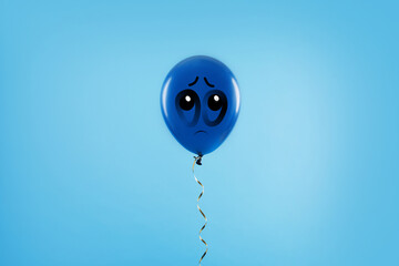 Blue balloon with sad face on light blue background