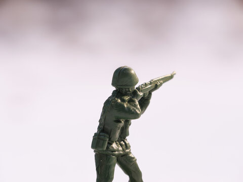 A war toy soldier captured in a close-up shot, illuminated by bright daylight on a cold, white snowy battlefield. The background features frozen snow, blurred.