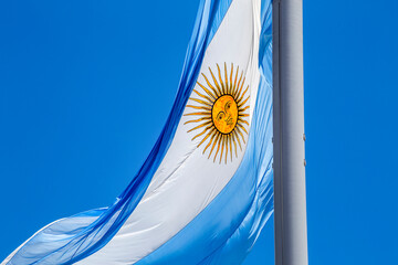 Argentine flag flying on a flagpole against a blue sky on a sunny day. Patriotic symbol of...