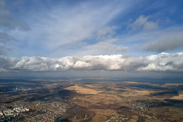 Aerial view from high altitude of distant city covered with puffy cumulus clouds flying by before...