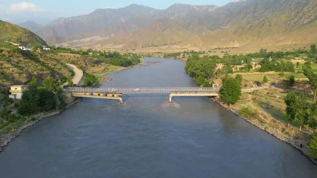 An aerial shot of a bridge crossing a river in a green village, The location is Kunar, Afghanistan.