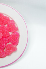 Valentine's Day concept: red heart shaped jelly beans sugar coated on rounded white with pink line on edge of plate stock photo copy space