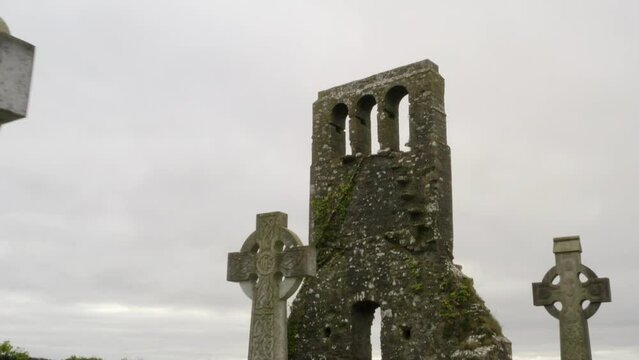 Push in past rounded cross stone headstones of graveyard with moss covered brick wall tower of old church