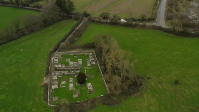 Panoramic aerial overview above graveyard off secluded countryside road in green pastures