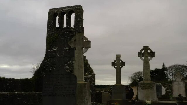 Ground level pan across old historic cemetery headstones with creepy old bell tower wall
