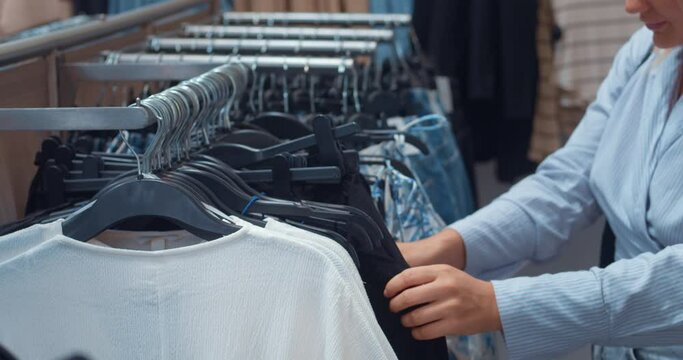 Woman shopping in clothing boutique. Style and trends woman stands among rows of clothing store looking for new favorite outfits choosing pants jeans t-shirts. Shopping mall sale concept black friday
