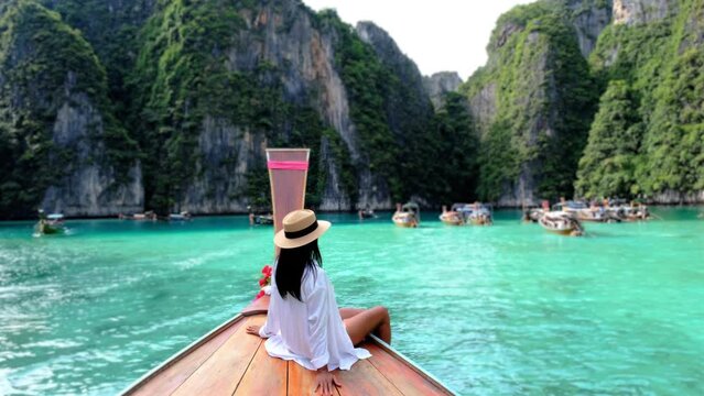 Asian women in front of a longtail boat at Kho Phi Phi Thailand, women in front of a boat at Pileh Lagoon with turqouse colored ocean during a boat trip to Maya Bay Koh Phi Phi 
