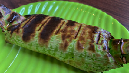 Nasi bakar daun or grilled rice on banana leaves isolated on cement background. This rice is wrapped by using banana leaf and then roasted by using charcoal. Ingredients with seafood, meat, chicken