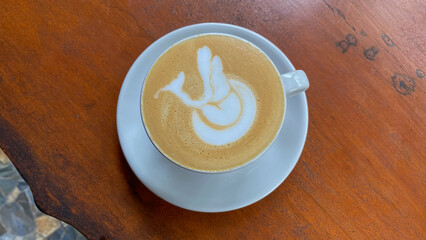 Cup of coffee latte with swan shape on old wooden background. White cup of Banyuwangi coffee bean