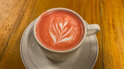 Cup of red velvet latte with leaf shape on old wooden background. White cup