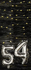 Silver foil balloon number 54 on a background of black tinsel with gold confetti. Birthday card,...