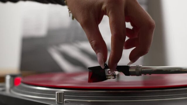 Record player being started and pick up being placed on a red vinyl record by female hand