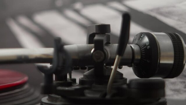 Close up of tone arm on record player being set down on a red vinyl record by female hand