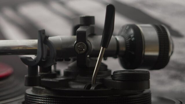 Close up of tone arm on record player being taken off a red vinyl record by female hand