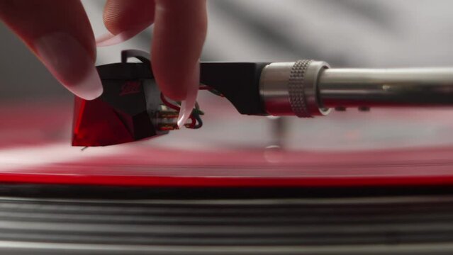 Super close up of record player pick up being set down on a red vinyl record by a female hand
