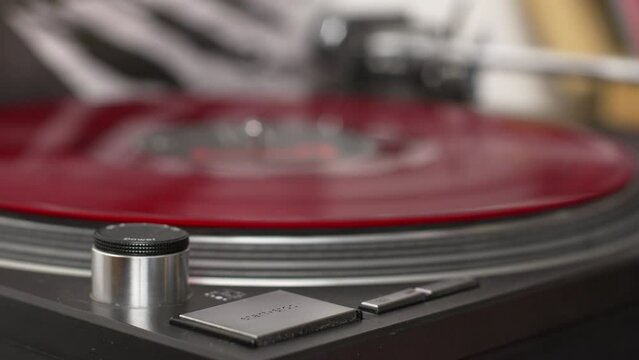 Record player with a red vinyl record being started and stopped by female hand