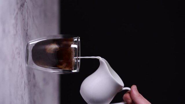 pouring milk in a transparent cup of coffee vertical video