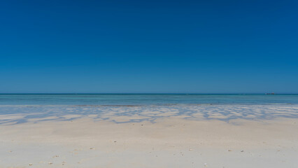 A paradisiacal minimalistic seascape. Sandy beach, aquamarine ocean, clear blue sky. Puddles and...