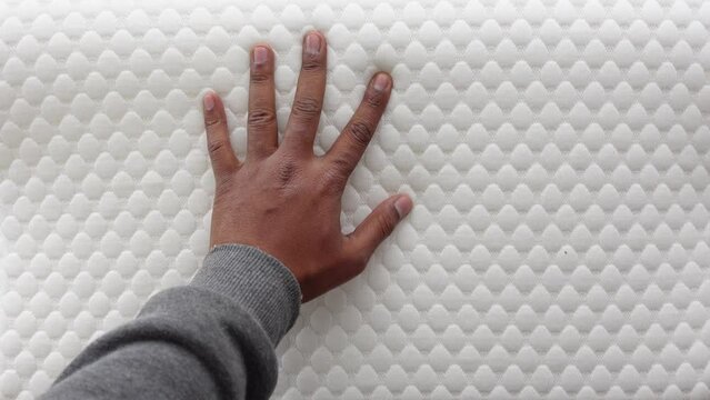 Hand touching and pressing orthopedic mattress on bed.