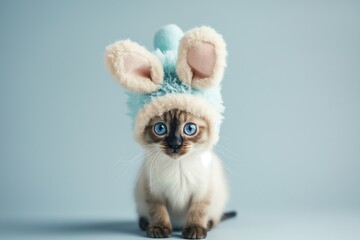 Obraz premium A cute cat, adorably dressed in a fluffy bunny ears hat, gazes upwards with big, soulful eyes against a soft grey background.