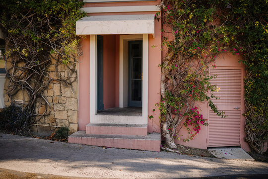 Sotogrante, Spain - January 26, 2024 -   pink house with a stone wall, overgrown with ivy and bougainvillea, a door, and a shuttered window.