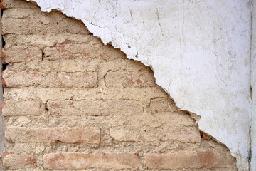 Red brick wall with grey cement plaster peeling and damaged