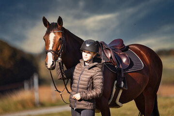 Horse stands with his rider on a meadow in the sun ready to ride out.