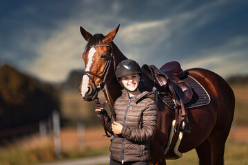 Horse stands with his rider on a meadow in the sun ready to ride out.