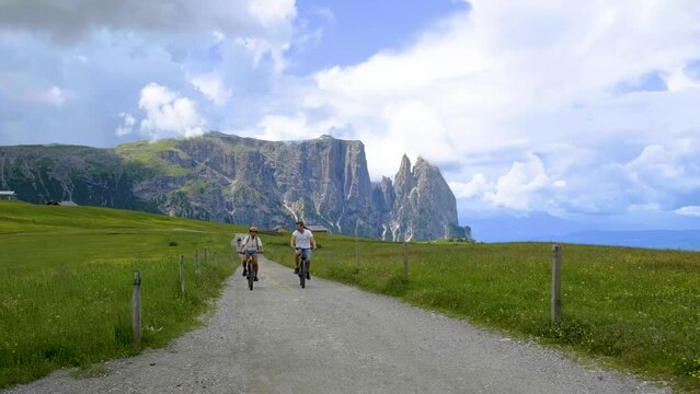 couple men and woman on vacation in the Dolomites Italy Alpe di Siusi, men and woman on Mountainbike Alpe di Siusi in beautiful morning light at sunrise in spring, South Tyrol