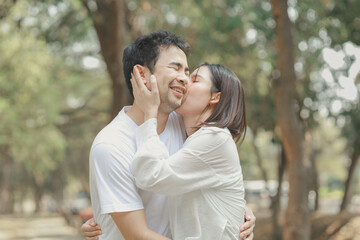 Naklejka premium Happy young Asian couple in a park, Portrait of smiling couple near beautiful nature outdoors, lifestyle, Cheerful couple hugging each other, Young couple enjoying the sunny day at park