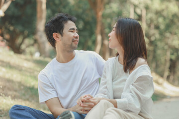Obraz premium Happy young Asian couple in a park, Portrait of smiling couple near beautiful nature outdoors, lifestyle, Cheerful couple hugging each other, Young couple enjoying the sunny day at park