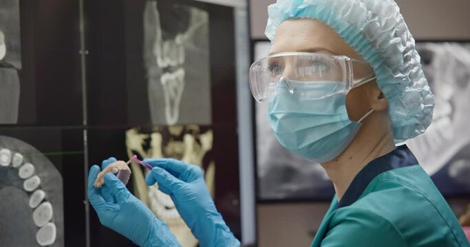 Orthopedic dentist doctor holds teeth 3d printed model of the patient's jaw on x-ray background