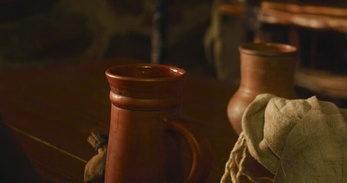 Medieval servant puts beer mug on wooden counter closeup. Barkeeper serves alcohol drinks in clay dishware in tavern. Drinking wine in old fashioned pub