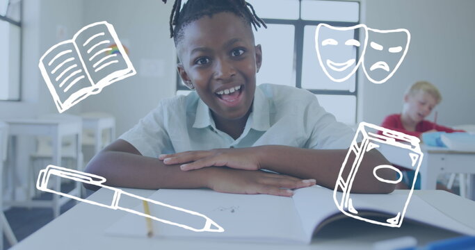 Image of literature icons over happy smiling african american schoolboy at desk in class