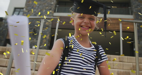 Image of gold confetti over happy caucasian schoolgirl with diploma and mortar board