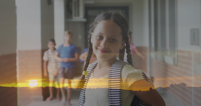 Image of sunset landscape over smiling biracial schoolgirl in school corridor - Powered by Adobe