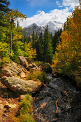 A creek on a forested valley surrounded by early fall foliage and snow-dusted peaks on the hike to Dream Lake, Rocky Mountain National Park, Estes Park, Colorado, USA.