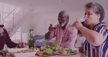 Image of confetti over diverse group of seniors drinking wine