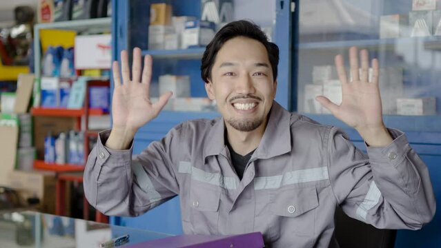 Portrait of young asian confident mechanic looking at camera along with making a cheeky face while sitting at a desk, concept confident, repair and maintenance service and garage expertise