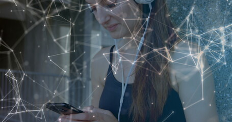 Network of connections floating against caucasian woman wearing headphones using smartphone