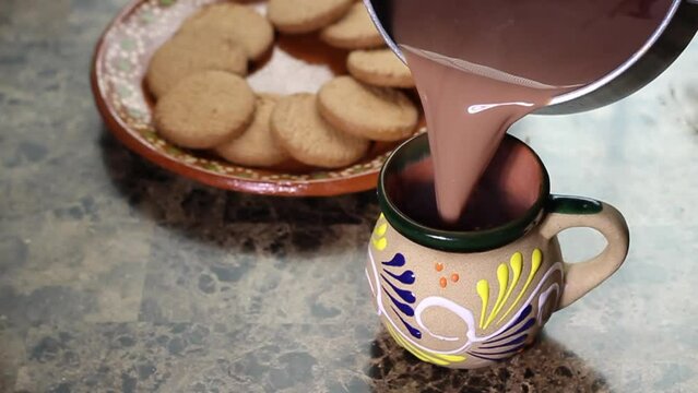 High angle view of person serving hot chocolate in traditional Mexican cup with cookies in slow motion. drink