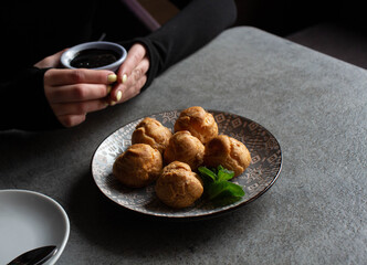 A girl drinks coffee and eats sweet profiteroles in a cafe