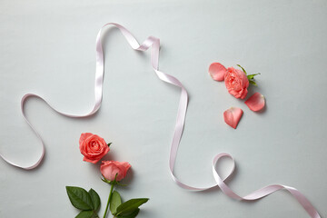 a beautiful pink rose and ribbon against a light grey blue paper background. top view. An empty...