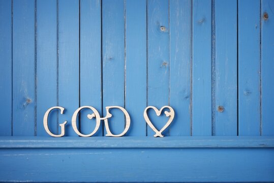 A blue painted wood background with the word God on it and a love heart