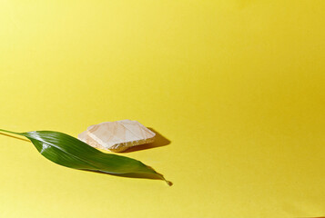 A marble square podium against light yellow background. With the stem of a flower. An empty platform for display cosmetic products, food and props.
